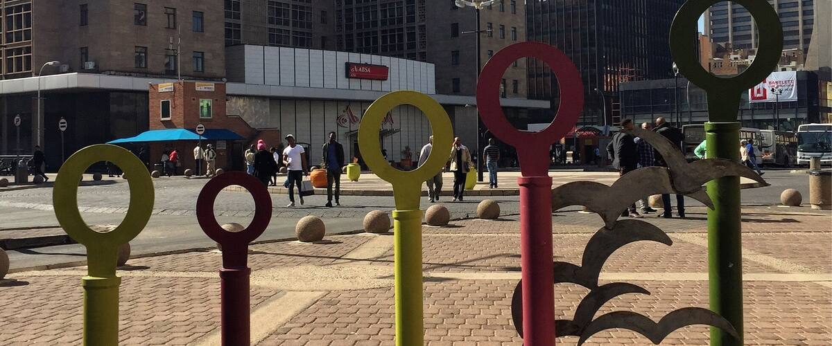 One end of Ghandi Square. There are bus stops on both sides, a statue of Ghandi, and plenty of shops.