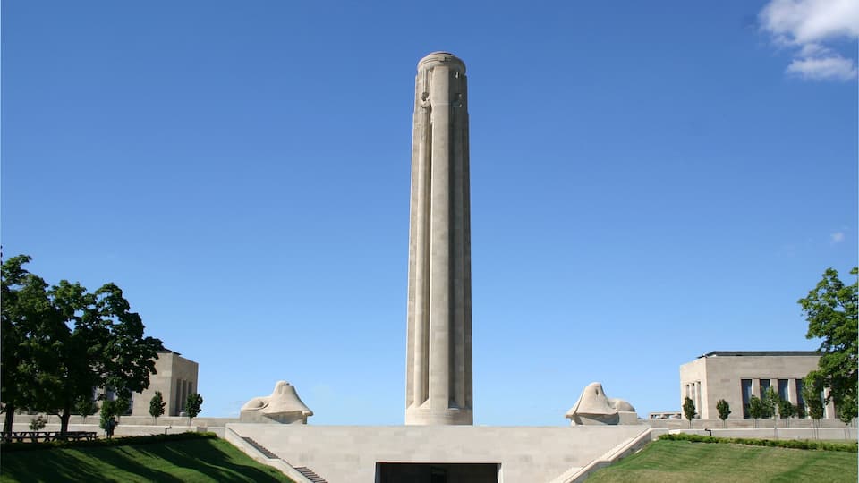 A tall, cylindrical monument with a base and steps leading up to it, surrounded by a well-maintained lawn and trees.