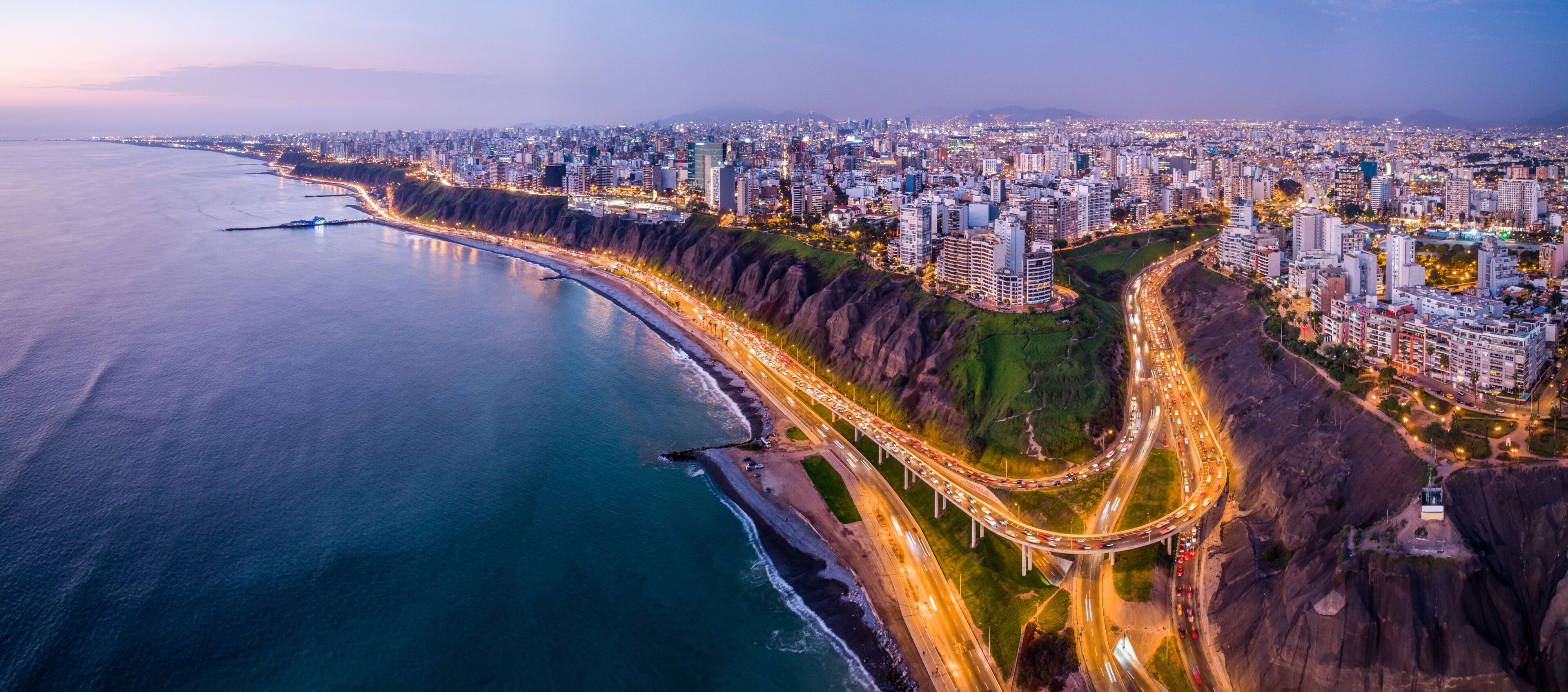 Un paisaje urbano costero con una autopista destacada que serpentea a lo largo de la costa, edificios urbanos densos y una vista despejada del océano.
