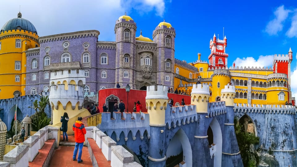 A colorful castle with yellow and purple walls, a red tower, and a blue bridge.