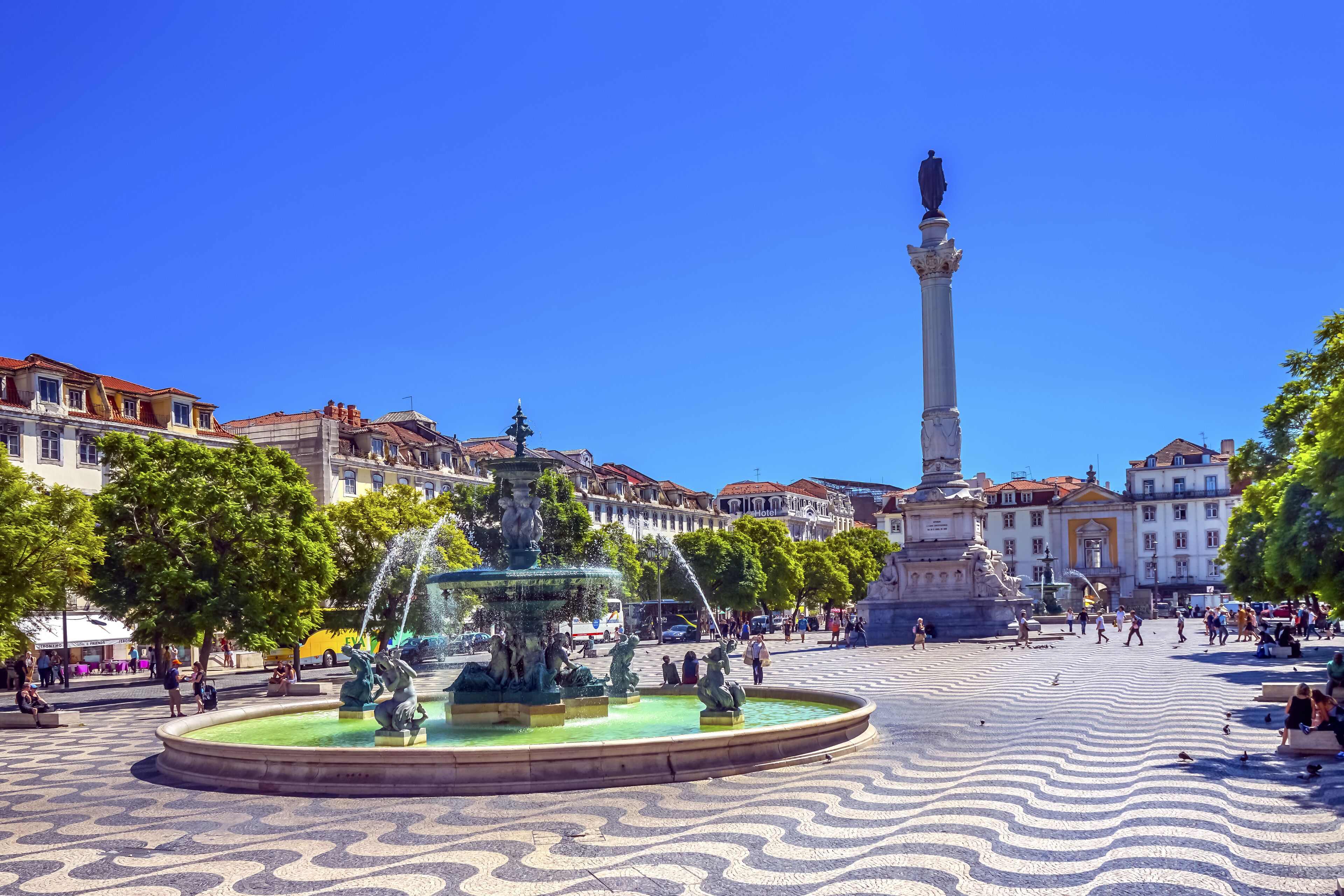 A public square with a fountain, a statue, and surrounding buildings.