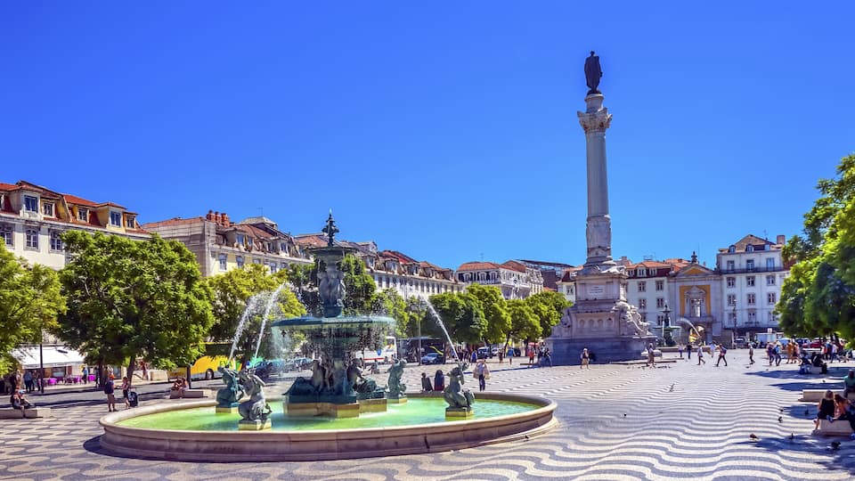 A public square with a fountain, a statue, and surrounding buildings.