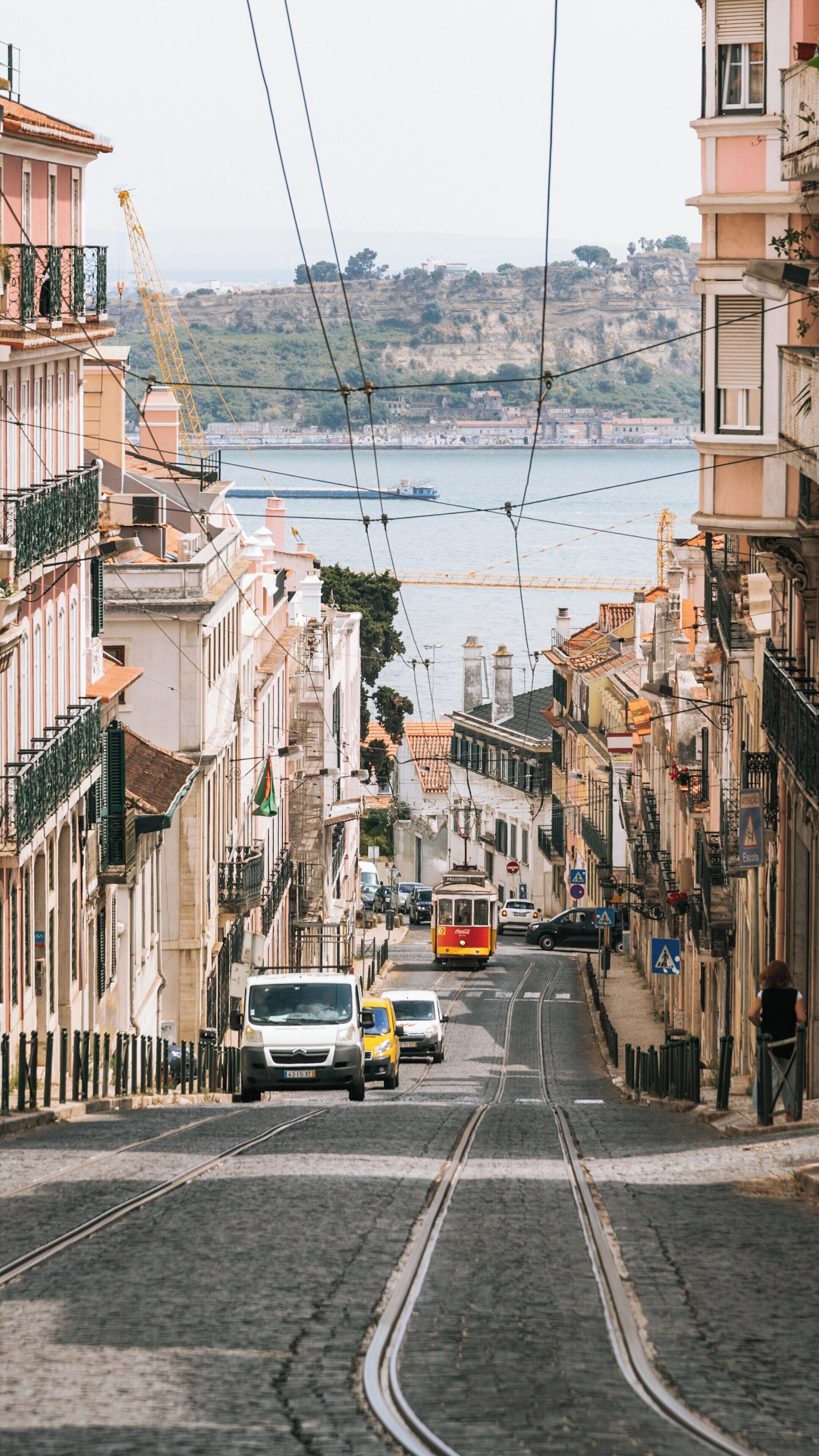 Una calle con tranvía, edificios y una masa de agua al fondo.