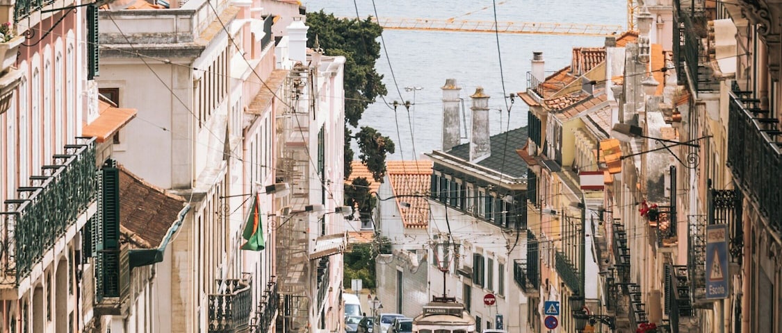 Una calle con tranvía, edificios y una masa de agua al fondo.