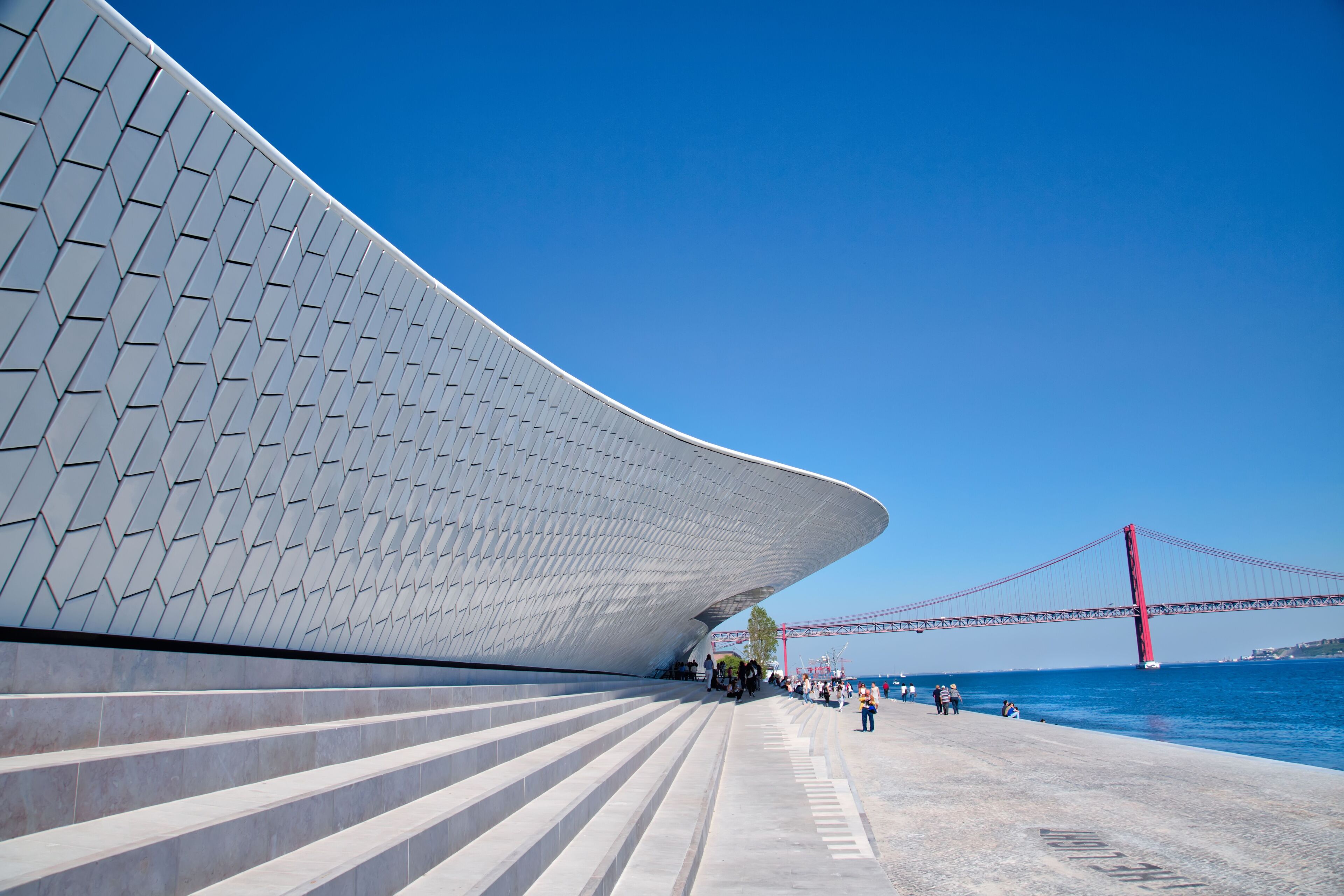 A modern architectural structure with a curved facade and a red bridge in the background.