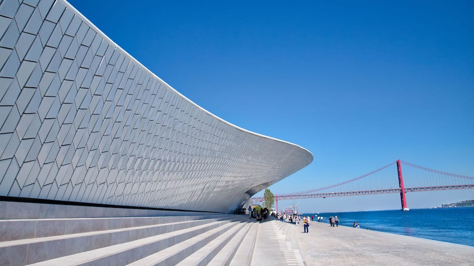 A modern architectural structure with a curved facade and a red bridge in the background.