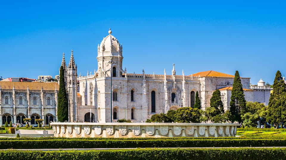 A historic cathedral with a prominent dome and intricate architecture, surrounded by well-manicured gardens and other historic buildings.