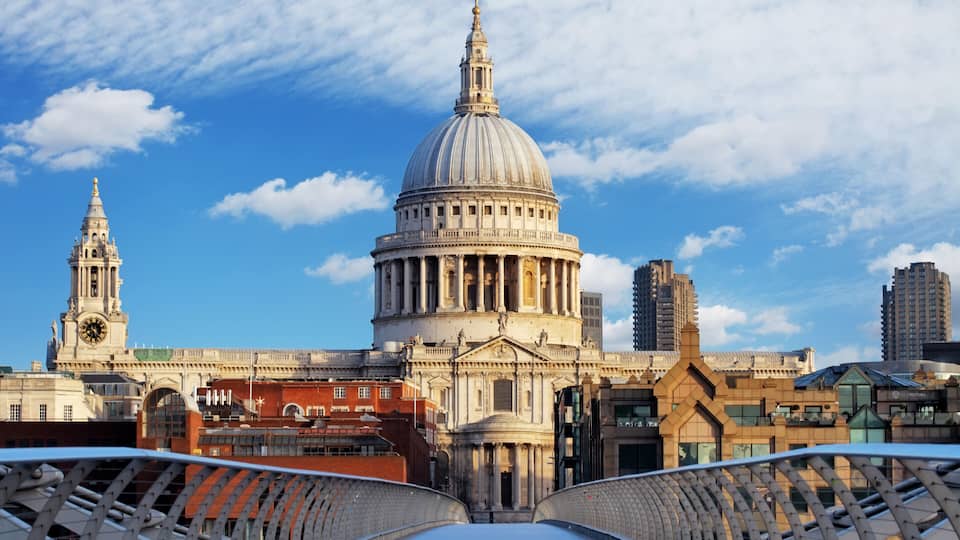 A large domed building with a clock tower, surrounded by modern buildings and a bridge.