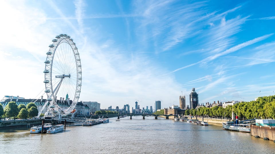 A river with a large Ferris wheel, a bridge, and a city skyline in the background.