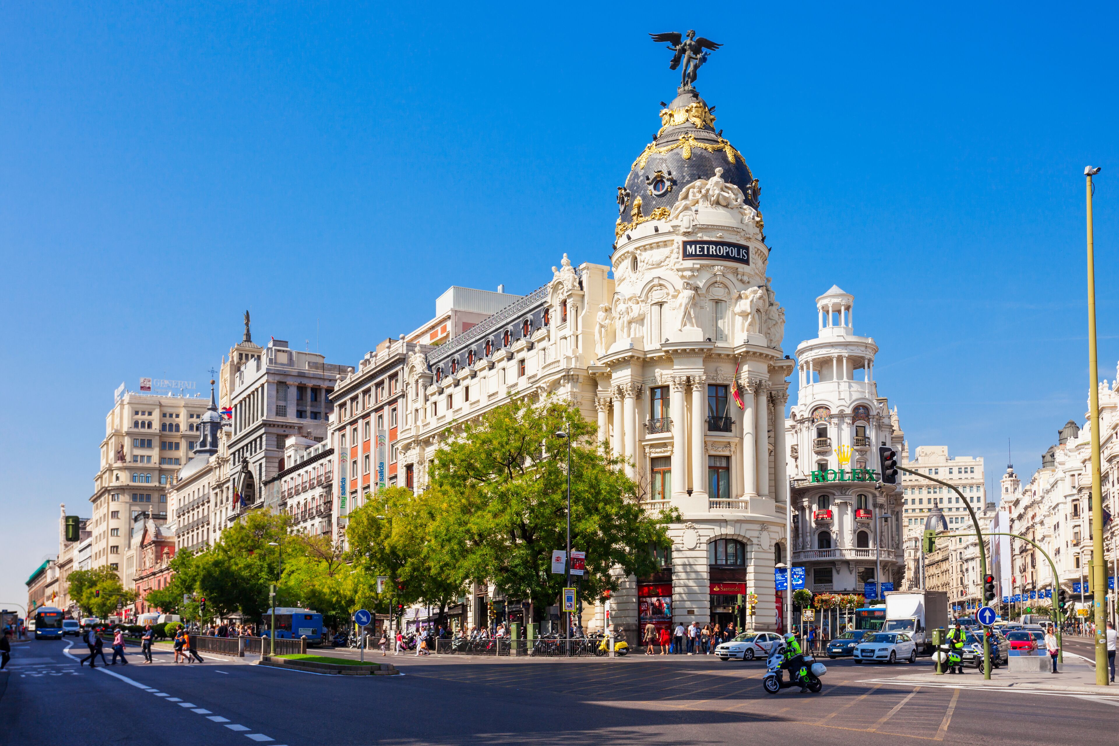 A busy urban street with historic buildings, including a prominent white building with a golden dome and the word "METROPOLIS" on it.