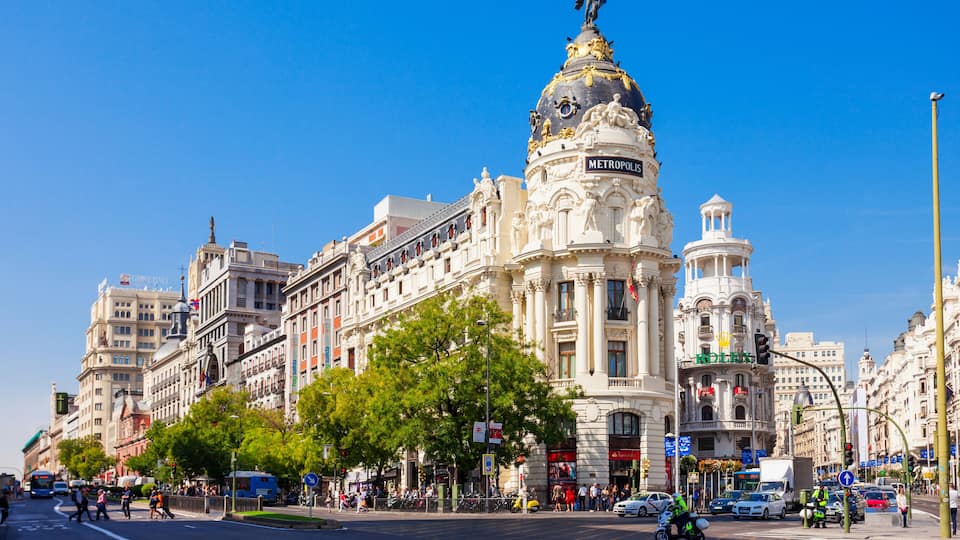 A busy urban street with historic buildings, including a prominent white building with a golden dome and the word "METROPOLIS" on it.