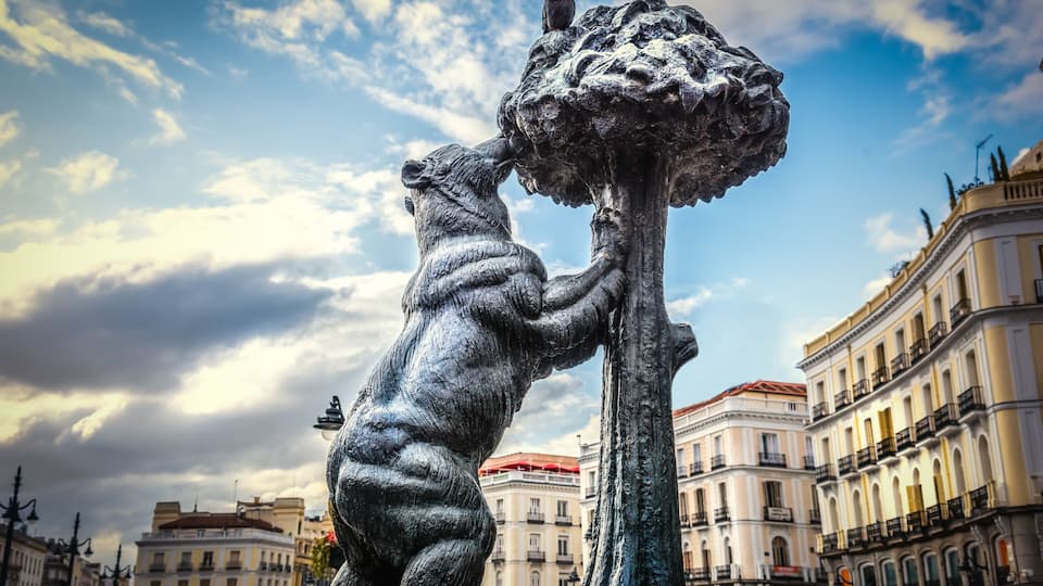 A bronze statue of a bear and a tree in an urban setting with historic buildings in the background.