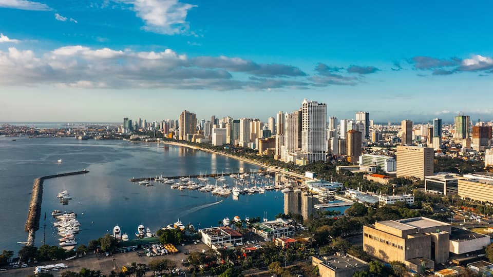A coastal cityscape with a marina, high-rise buildings, and a clear sky.