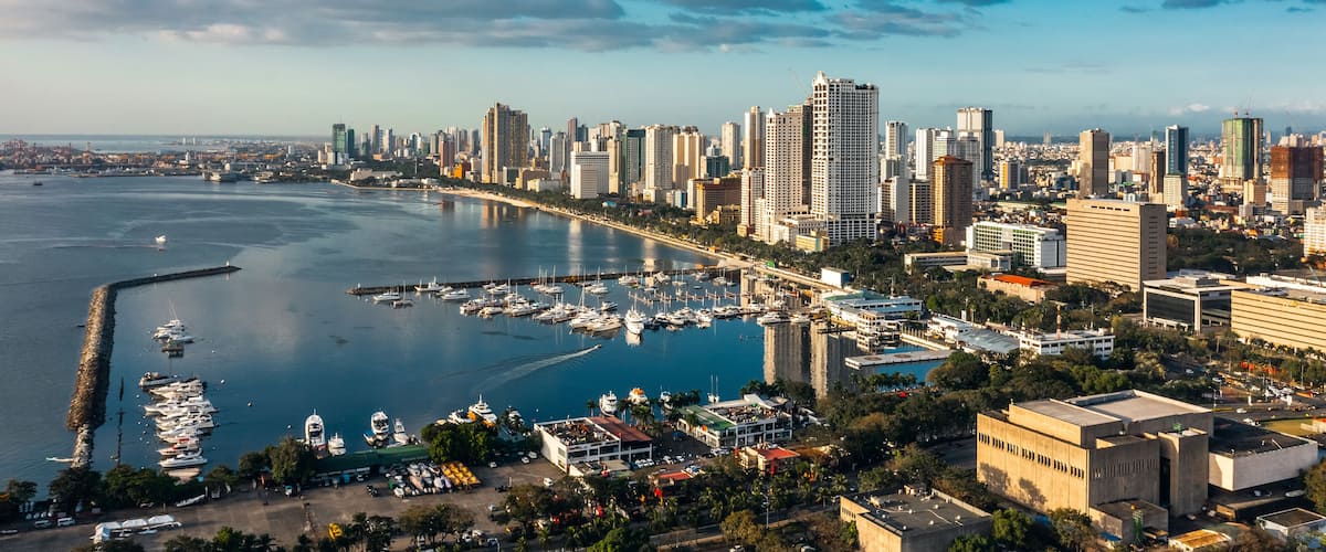 A coastal cityscape with a marina, high-rise buildings, and a clear sky.