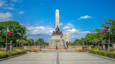 A monument with a statue, surrounded by trees and flags, under a clear blue sky.