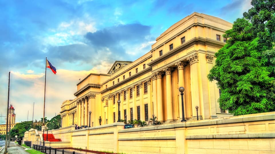 A large classical building with columns, a flag, and a tree.