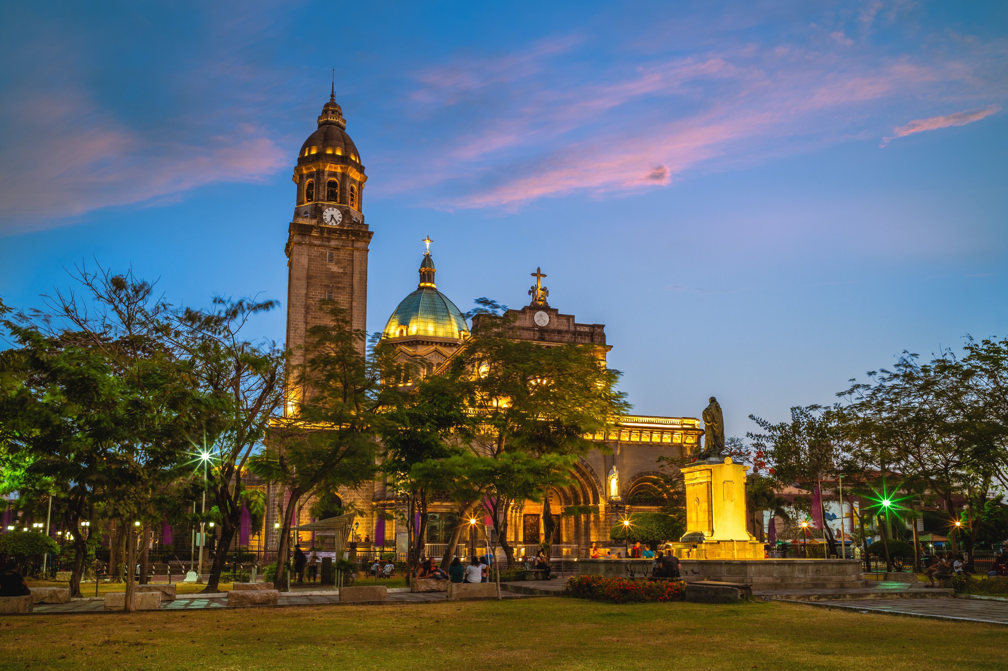 A historic building with a clock tower and a dome, surrounded by trees and a plaza.