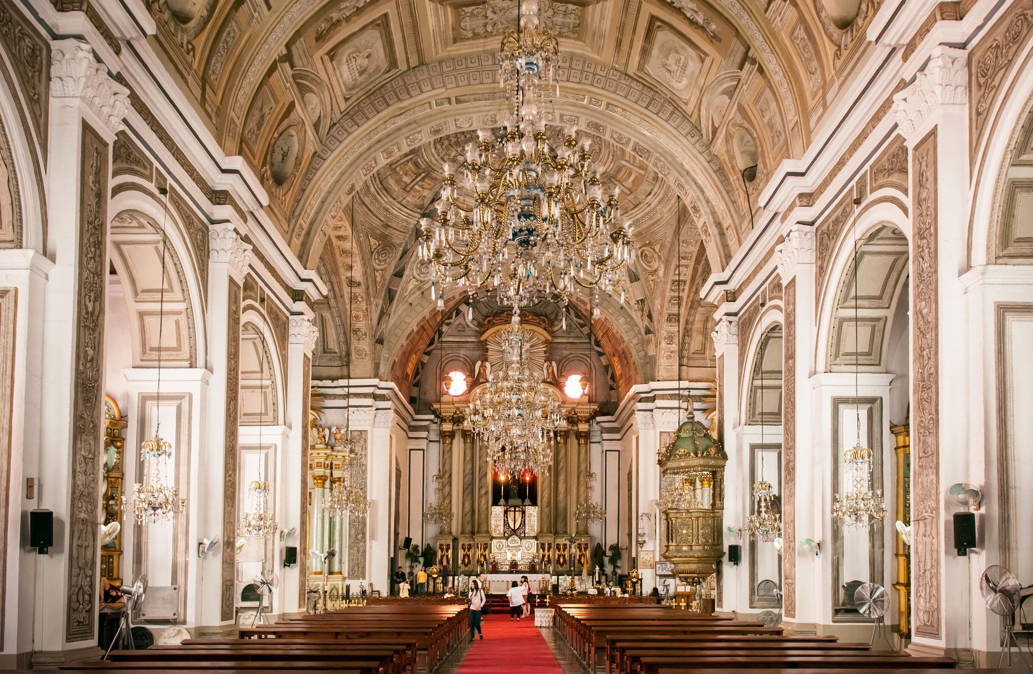 An ornate church interior with a large chandelier, arched ceilings, and rows of pews.
