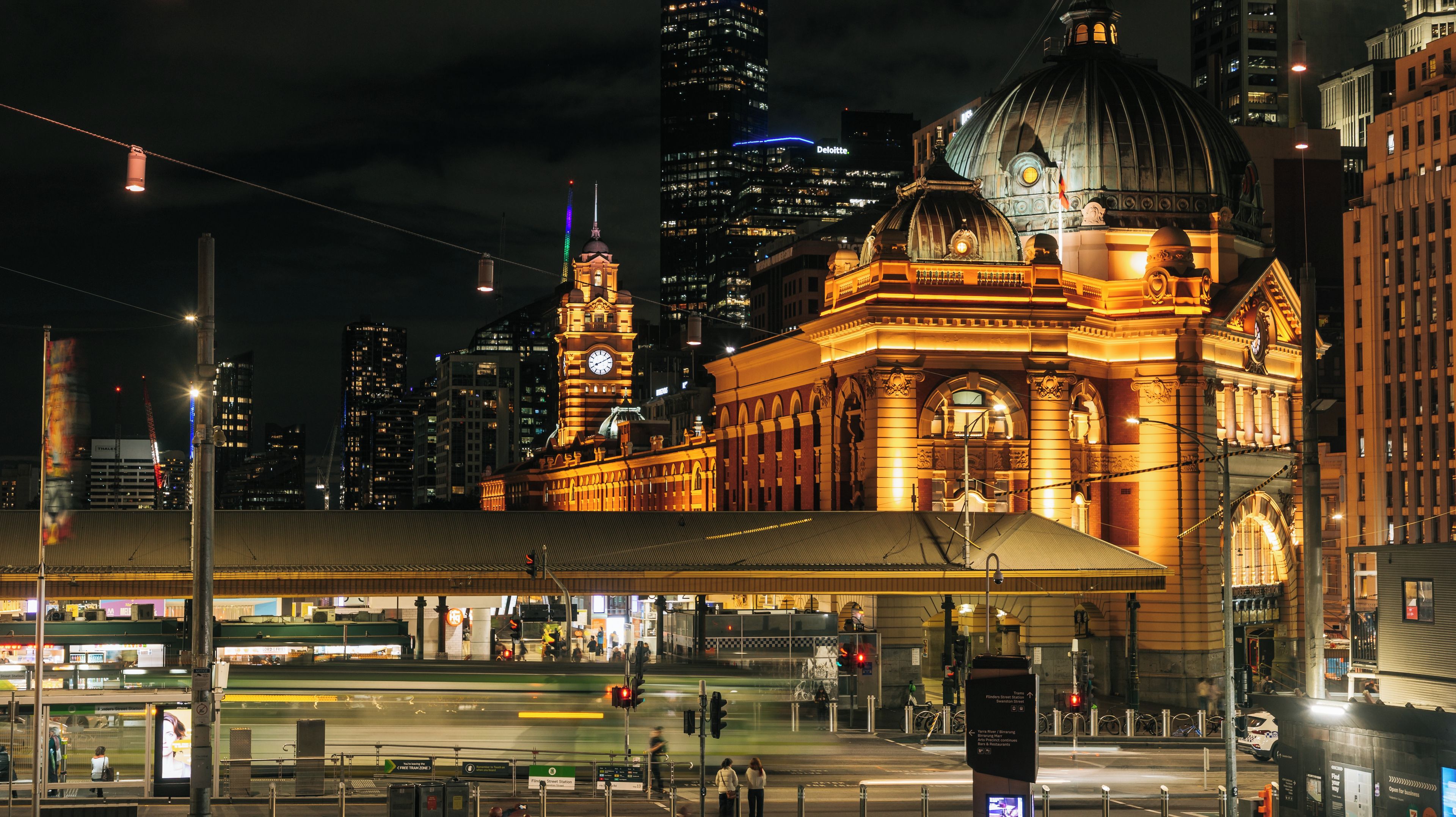 A brightly lit train station with a large dome and clock tower, surrounded by modern skyscrapers.