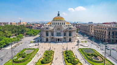 A large, ornate building with a golden dome and a statue on top, surrounded by a spacious plaza with well-manicured gardens.