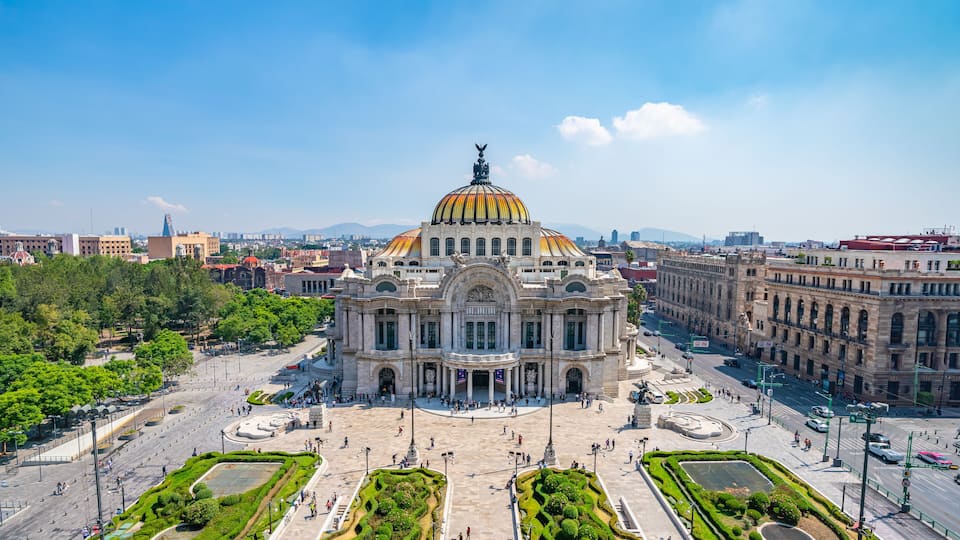 A large, ornate building with a golden dome and a statue on top, surrounded by a spacious plaza with well-manicured gardens.