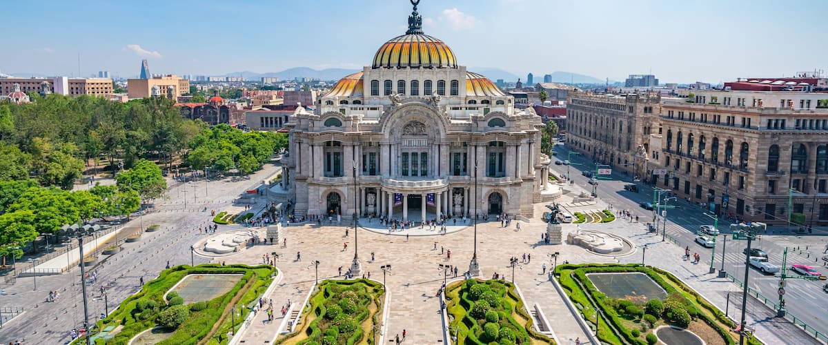A large, ornate building with a golden dome and a statue on top, surrounded by a spacious plaza with well-manicured gardens.