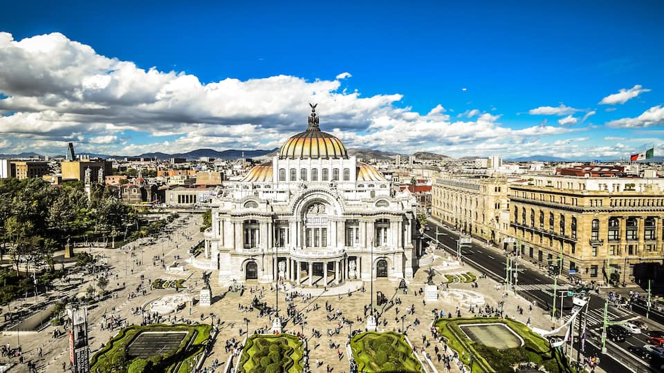 A grand building with a large dome, surrounded by a spacious plaza with people and greenery.