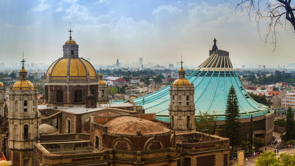 A historic cathedral with multiple domes and bell towers, a large green tent-like structure, and a cityscape in the background.