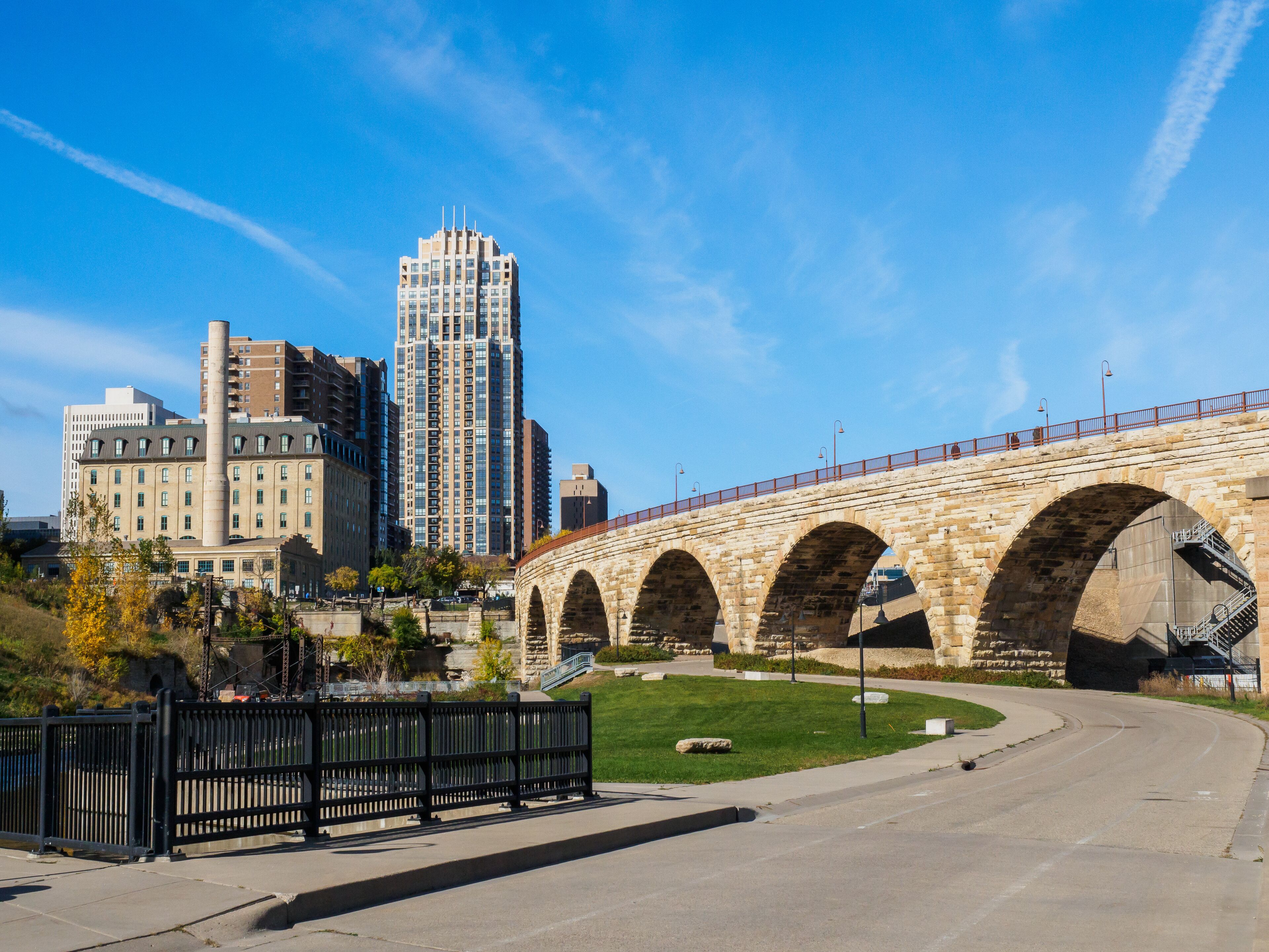 A stone bridge with arches, a modern building, and a clear blue sky.