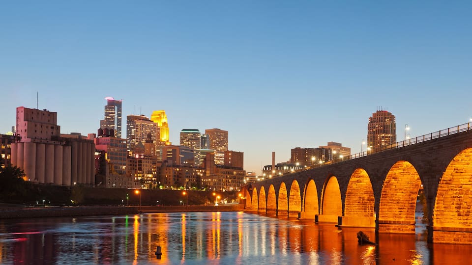 A city skyline with illuminated buildings and a stone bridge over a river.