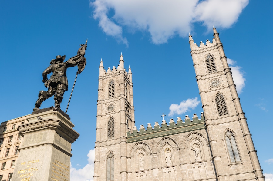 A statue of a historical figure on a pedestal in front of a large church with two towers.