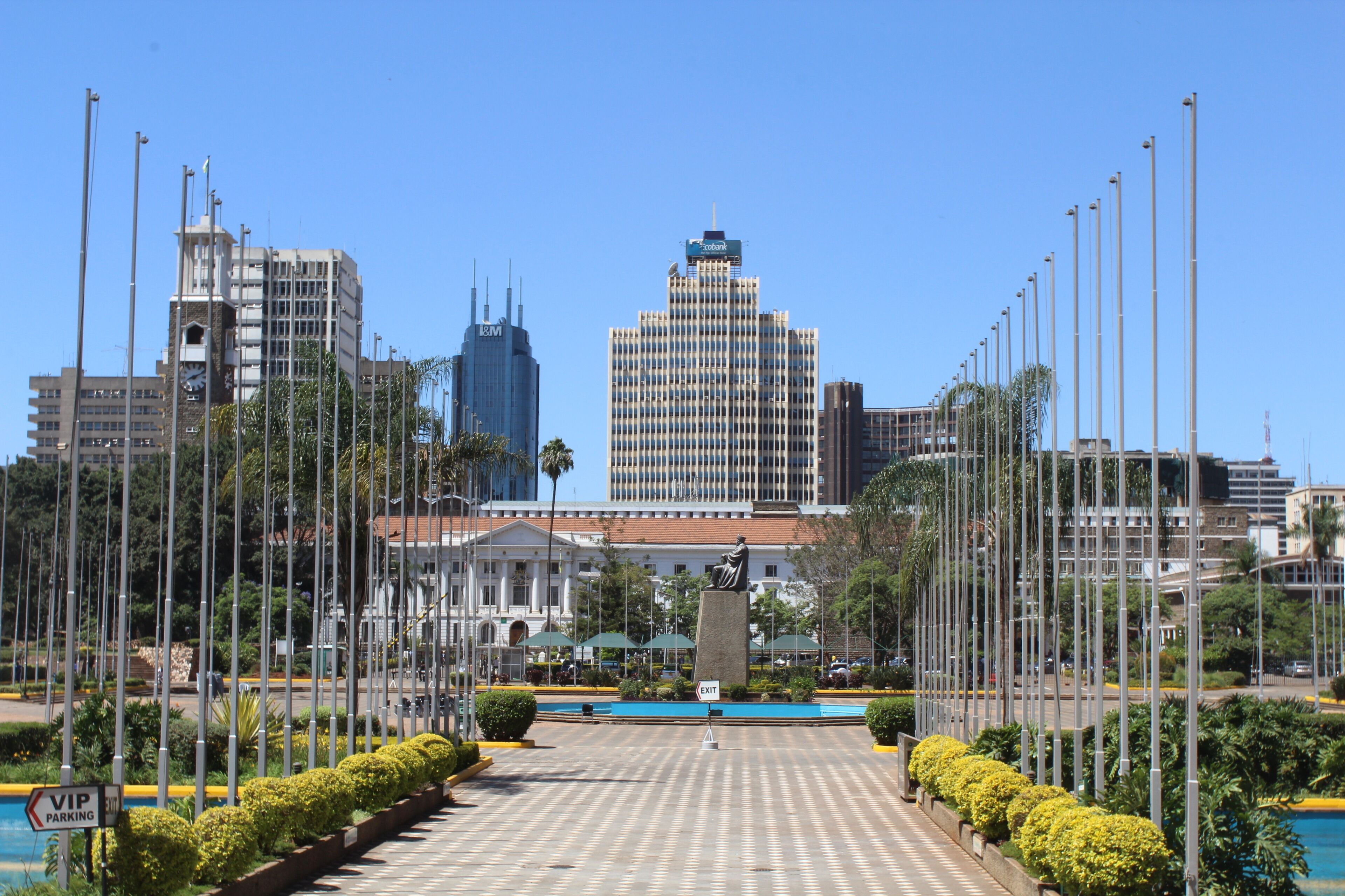 A city square with a statue, a fountain, and tall buildings in the background.