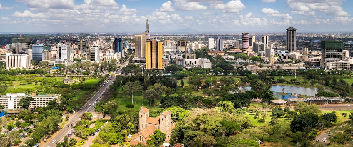 A cityscape with a mix of modern skyscrapers and historical buildings, surrounded by green parks and a large body of water.