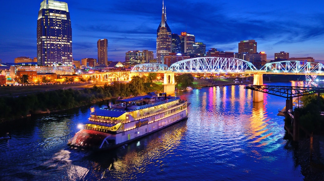 A river with a boat, a bridge, and a city skyline with illuminated buildings.