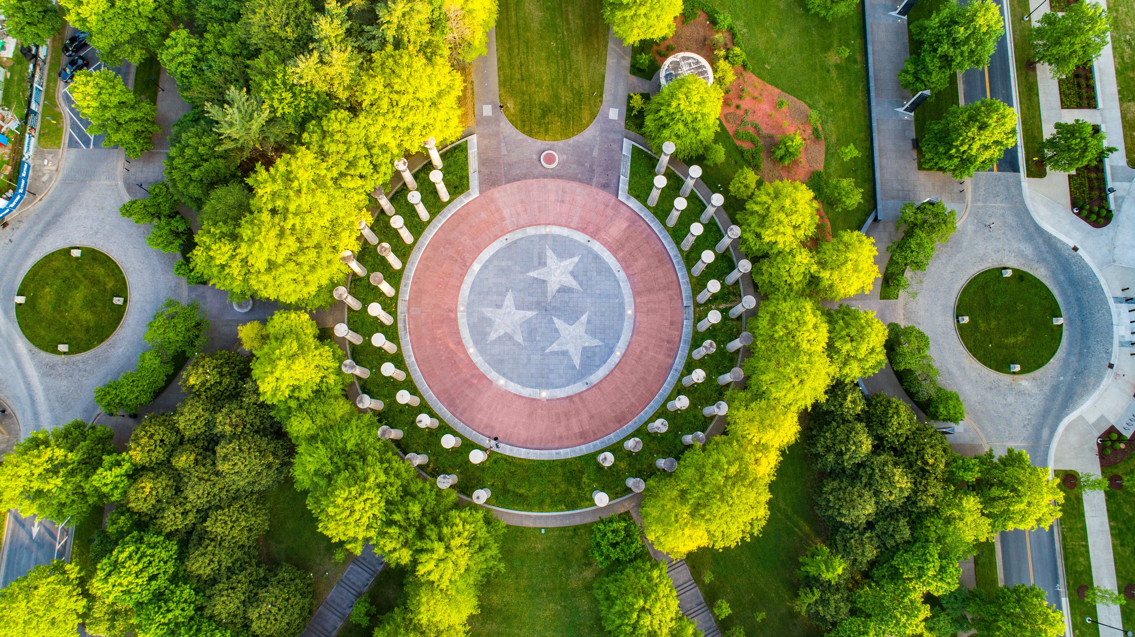 An aerial view of a circular plaza with a central star-patterned design, surrounded by trees and pathways.