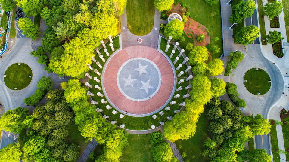 An aerial view of a circular plaza with a central star-patterned design, surrounded by trees and pathways.