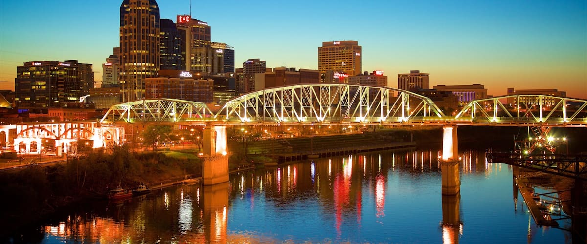 A city skyline with a prominent skyscraper and a brightly lit bridge over a river.