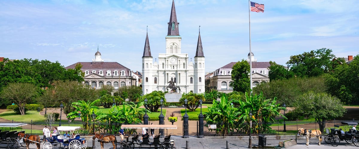 A historic church with three spires, surrounded by lush greenery and a flagpole with an American flag.