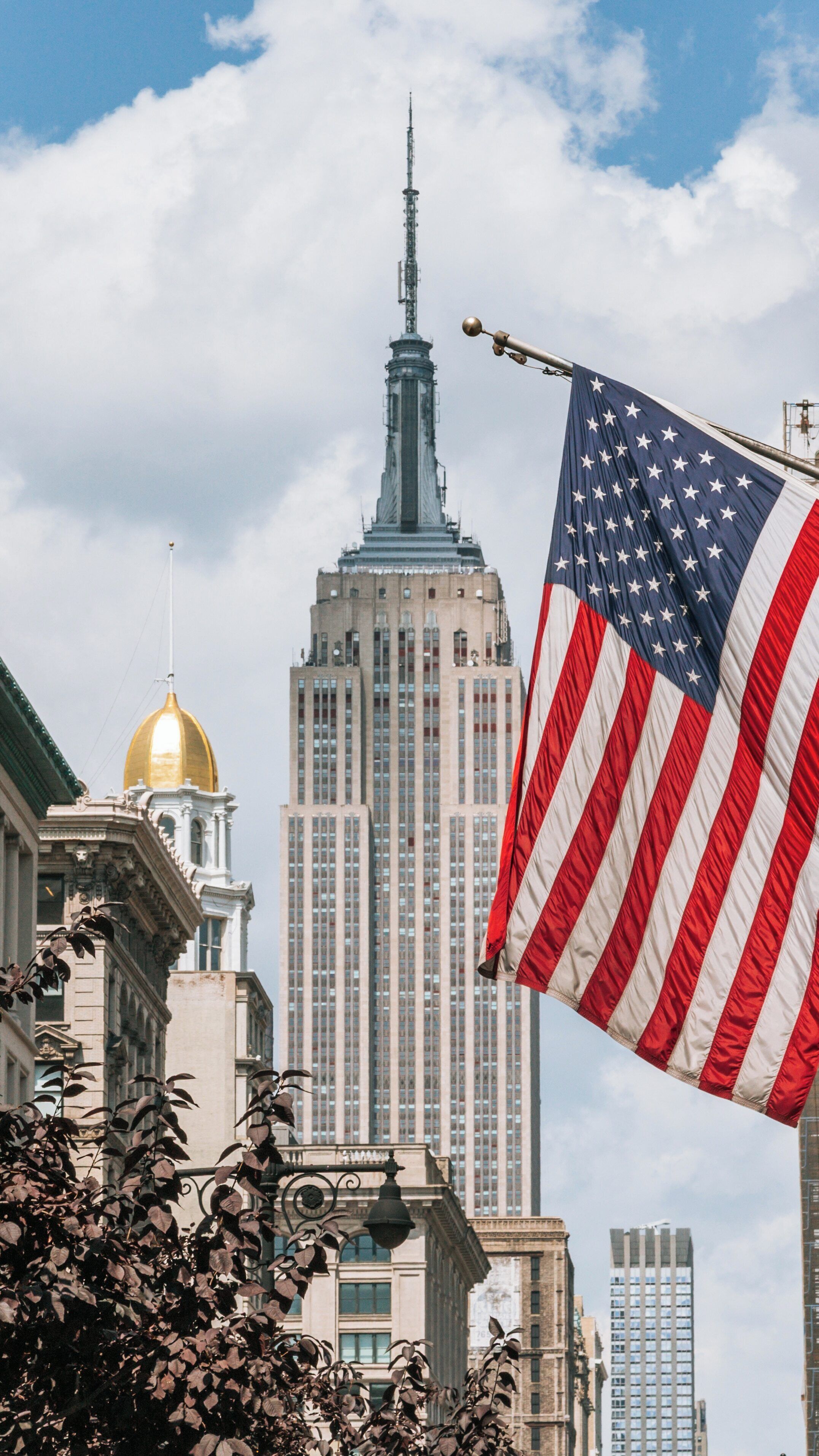 Skyline view of Empire State Building and American flag waving on 5th Avenue in Manhattan during a sunny day in New York City