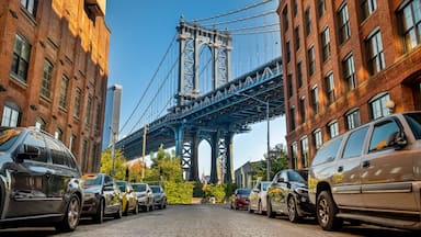 A street with parked cars and a large bridge in the background.