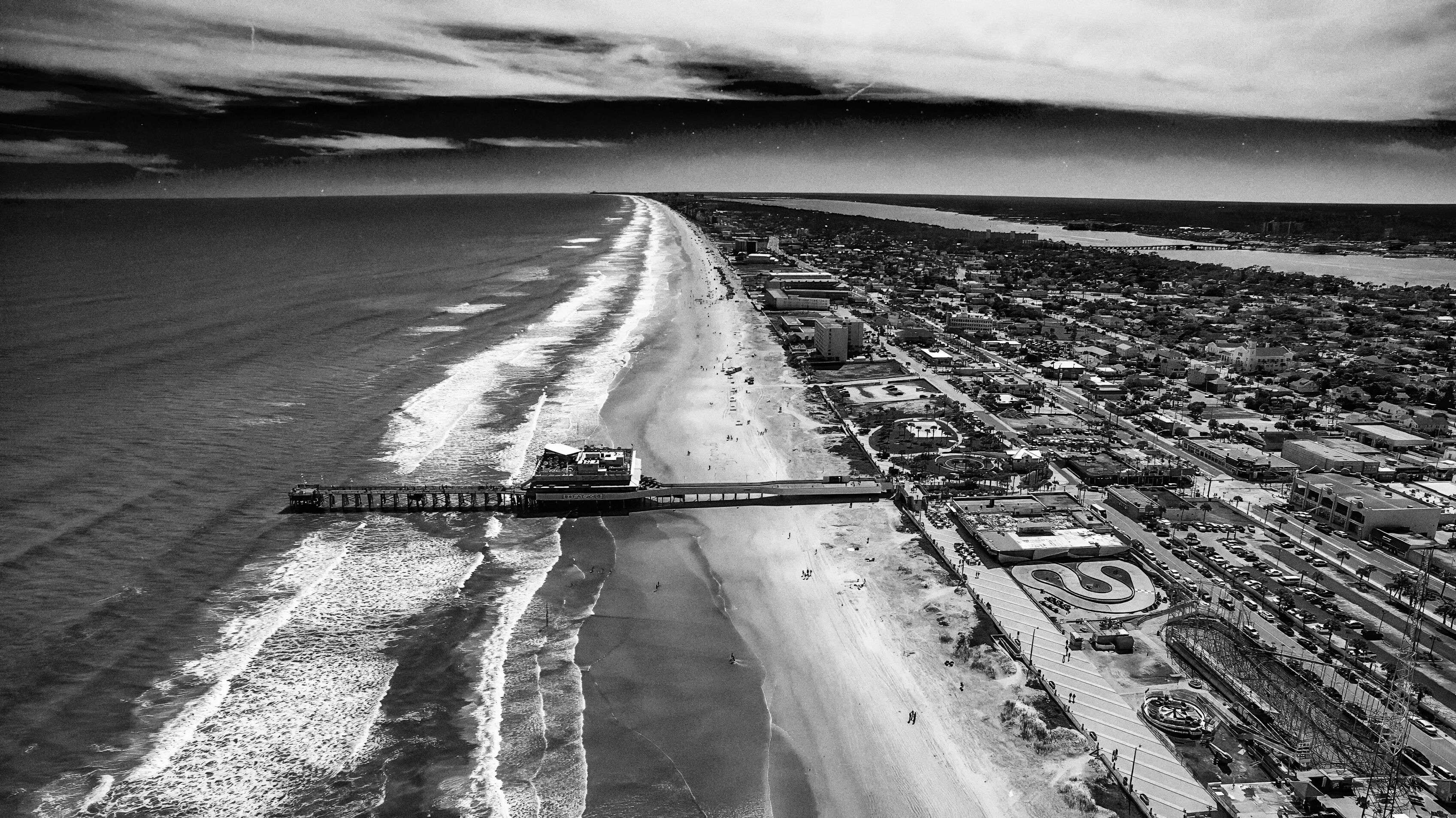 A coastal cityscape with a beach, pier, and urban area.