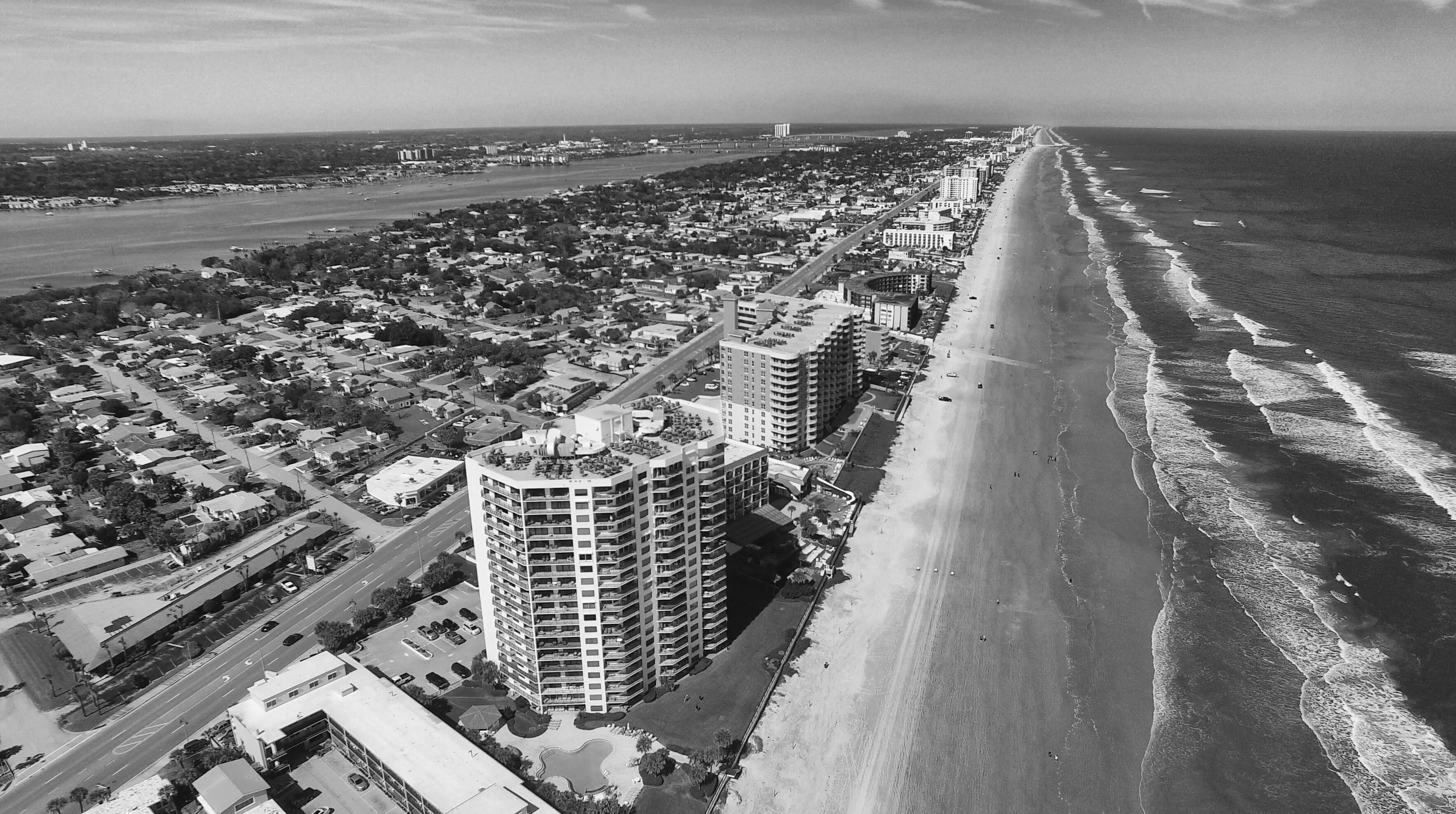 An aerial view of a coastal city with a long beachfront, high-rise buildings, and a dense urban area.
