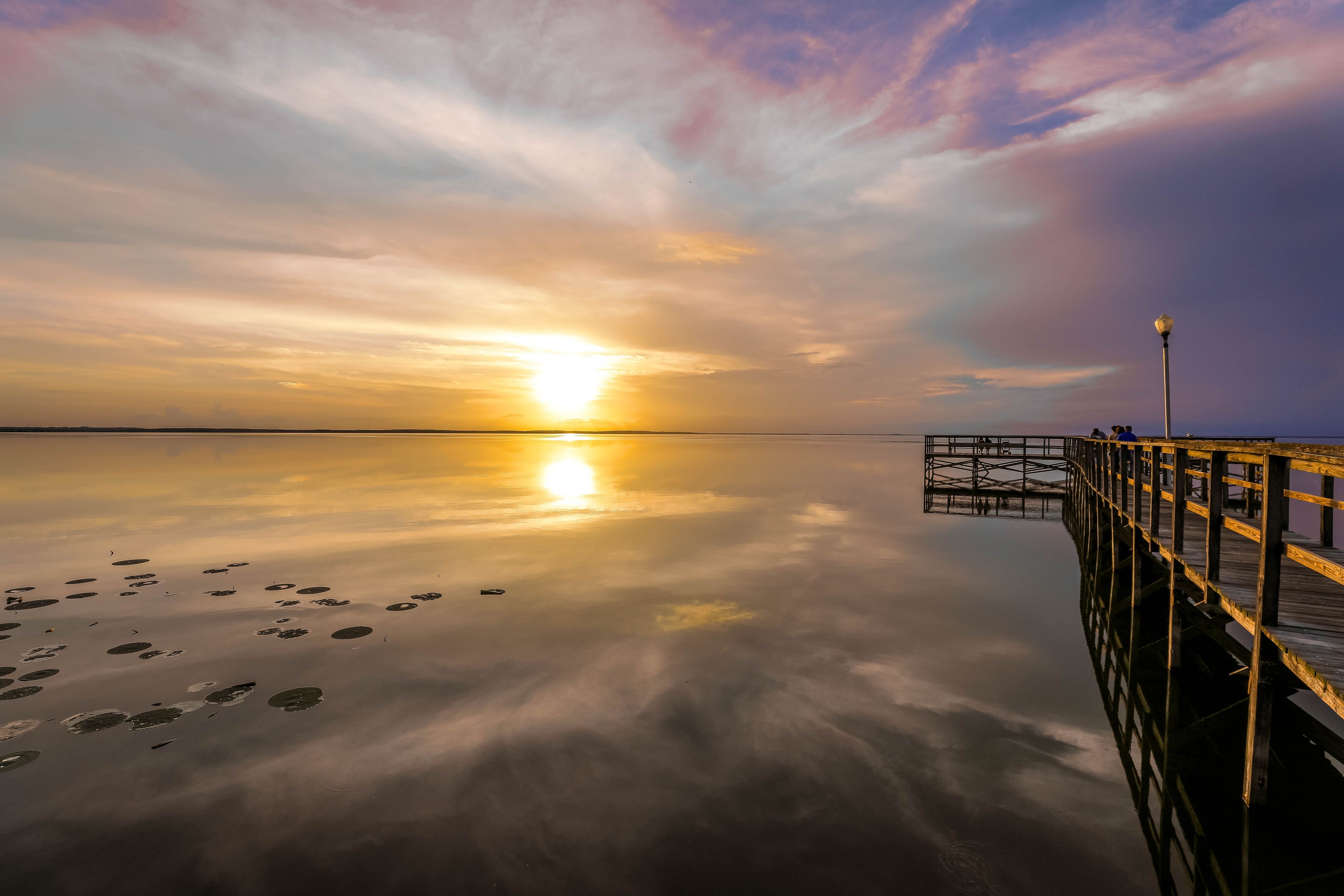 A calm lake at sunset with a wooden pier extending into the water.