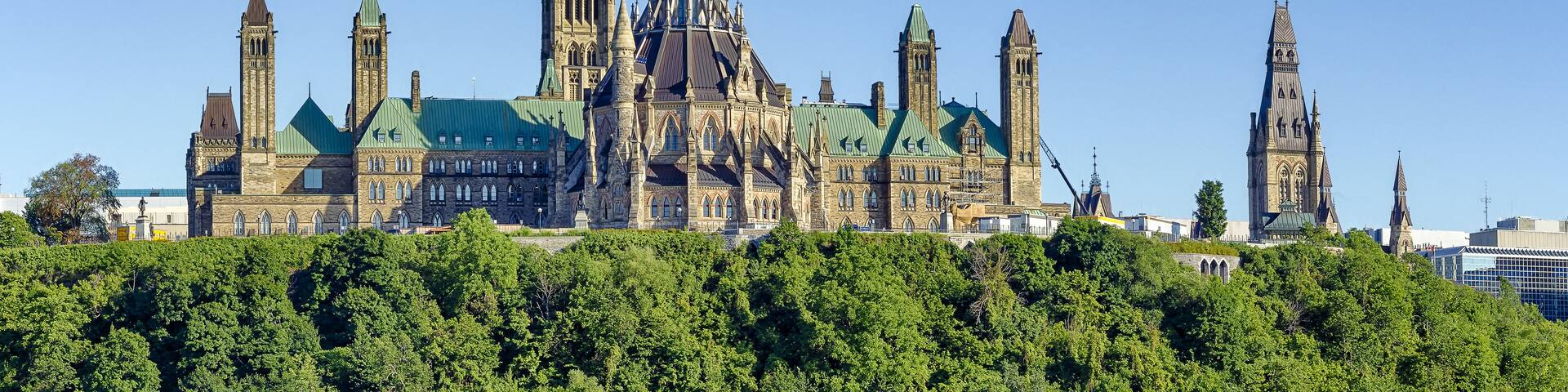 A historic building with multiple spires and a clock tower, surrounded by lush greenery.