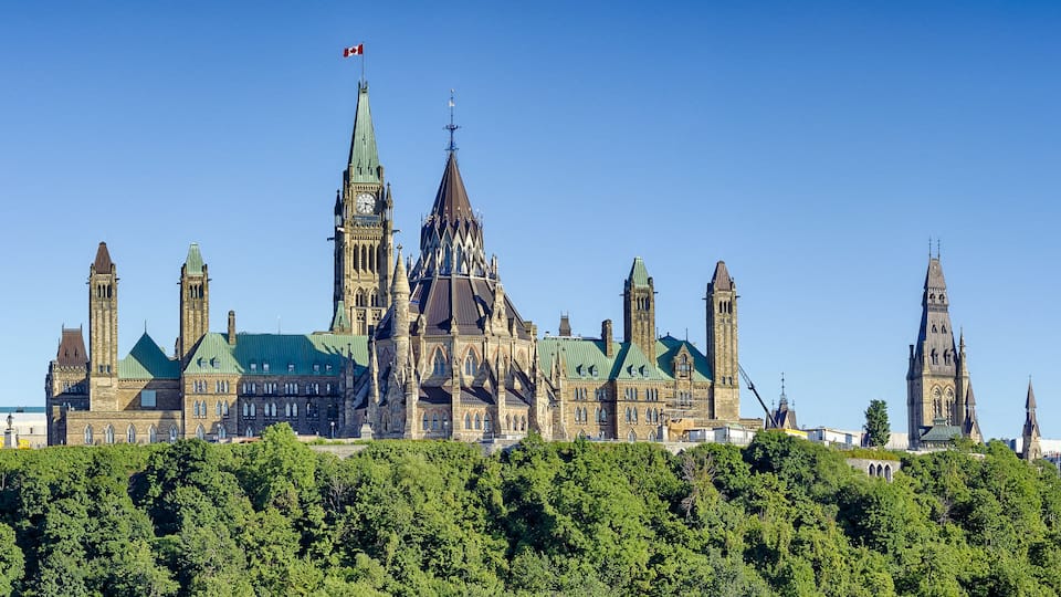 A historic building with multiple spires and a clock tower, surrounded by lush greenery.