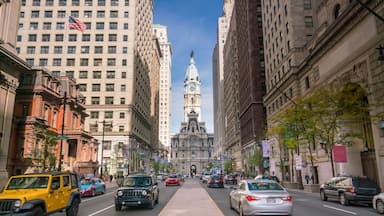 A city street with tall buildings, a prominent clock tower, and cars driving on the road.