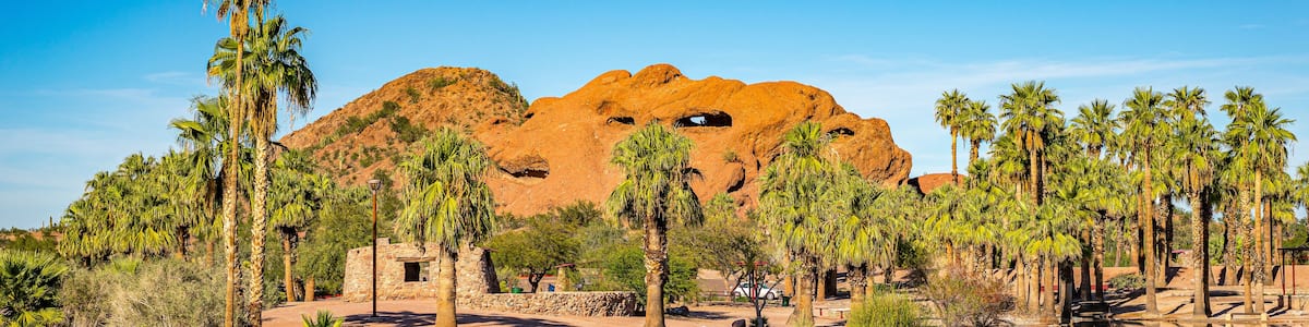 Un paysage désertique avec une grande formation rocheuse, des palmiers et une étendue d’eau qui reflète le paysage environnant.