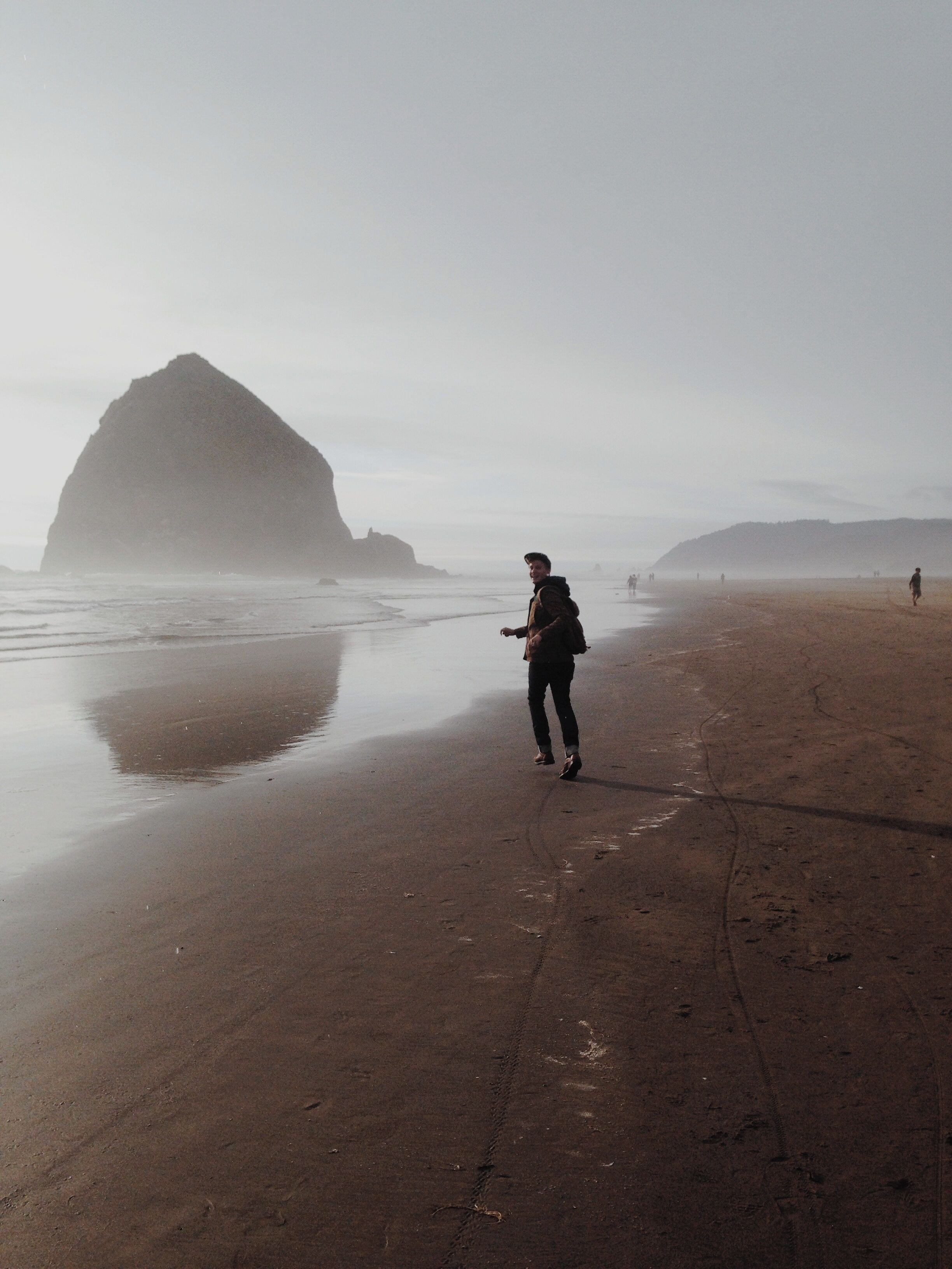 A person walking on a foggy beach with a large rock formation in the background.