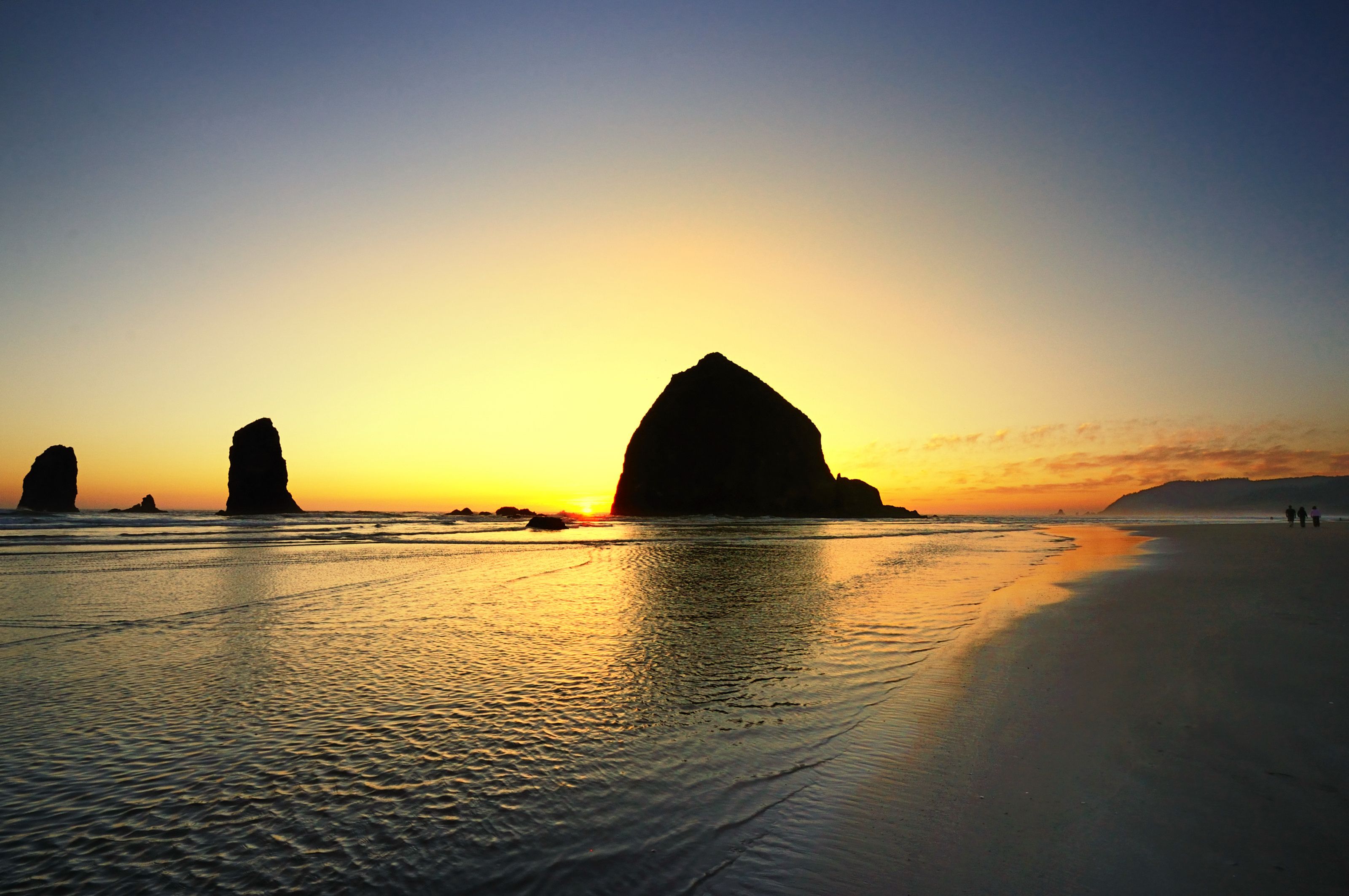A beach with large rock formations silhouetted against a sunset sky.
