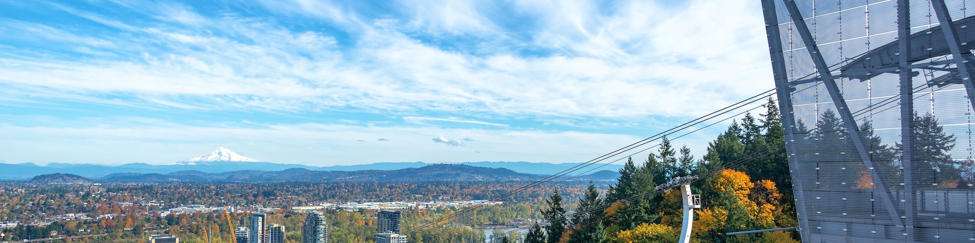 Teleférico em área arborizada, com paisagem urbana ao fundo, incluindo uma montanha imponente.